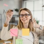 Female mentor showing thumb up while writing on board