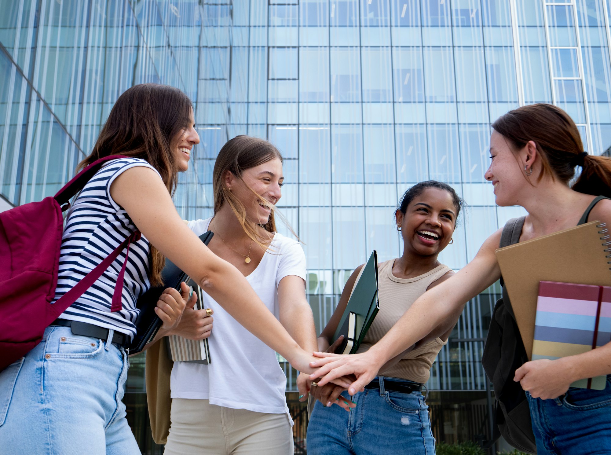 Group of four multi-ethnic student girls shake hands on a campus . Empowered women, feminism