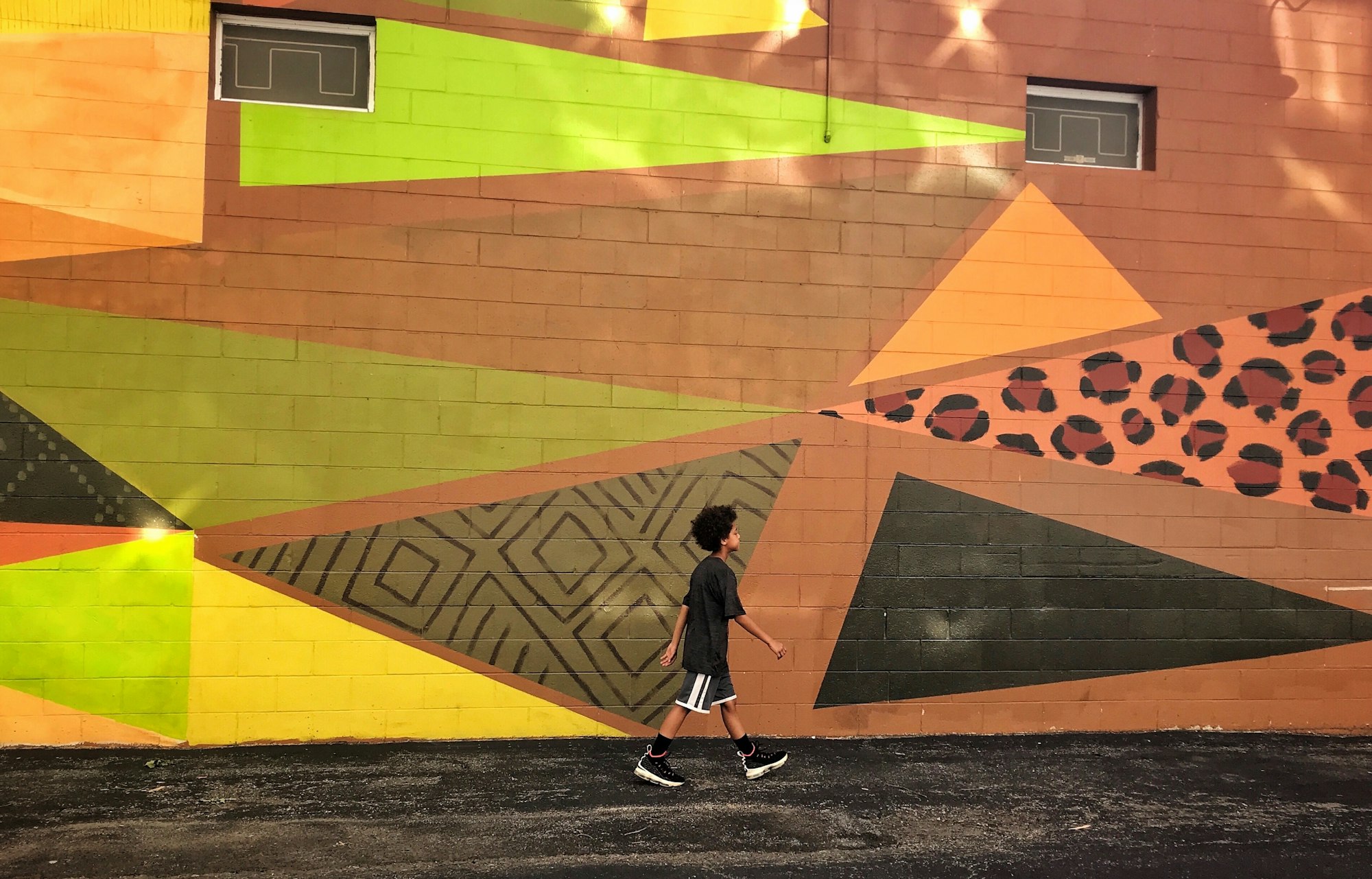 Mixed race boy walking past earth colored street art with geometric shapes